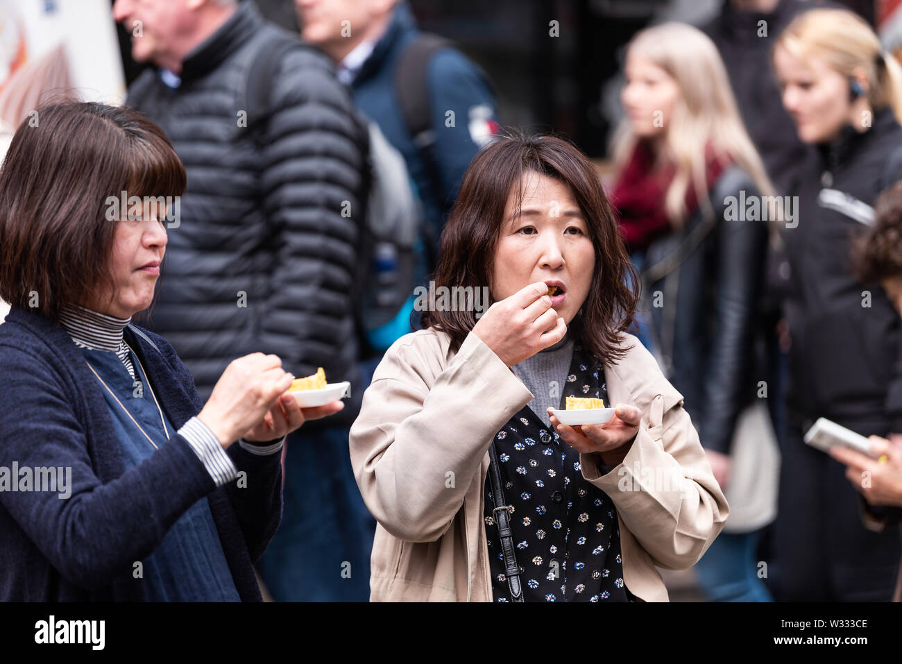 Tokyo, Giappone - 30 Marzo 2019: due Asian Le donne cinesi mangiare giapponese tamagoyaki uova frittata arrotolata in Ginza del pesce di Tsukiji street mercato esterno Foto Stock