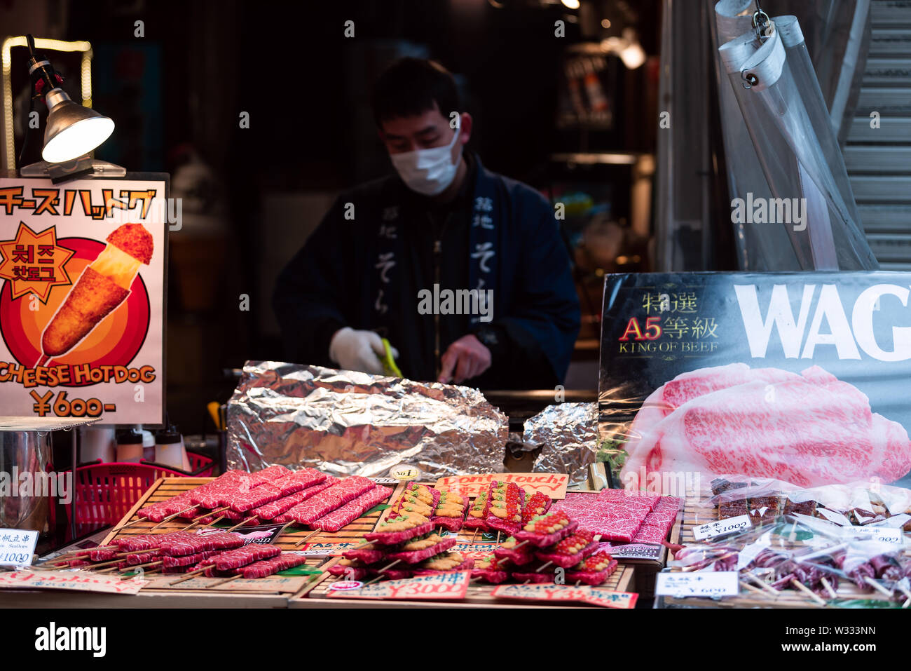 Tokyo, Giappone - 30 Marzo 2019: spiedini di carne di manzo wagyu, ricci di mare caviale su spiedini di Tsukiji esterno sul mercato del pesce di Ginza con uomo venditore la cottura della carne Foto Stock