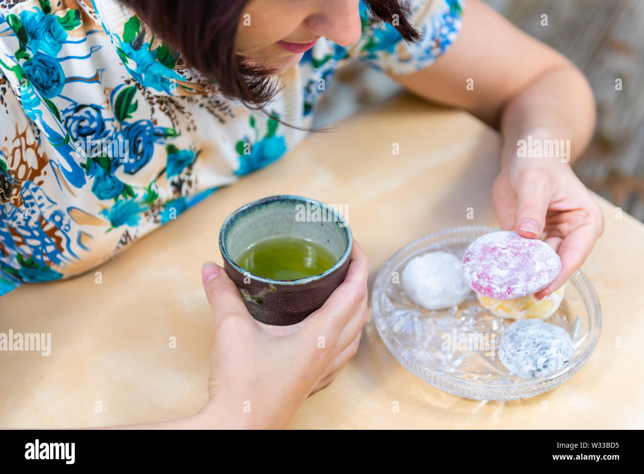 Donna di prelevare daifuku mochi e nero capelli asiatici seduti al tavolo da tè verde tazzina fuori in giardino nel cortile Foto Stock