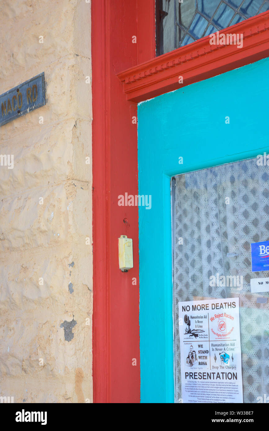 Un vecchio vetro porta anteriore con tendine in a sudovest di colori, con manifesti promuovere sentimenti umanitari e attivista informazioni in Bisbee, AZ Foto Stock