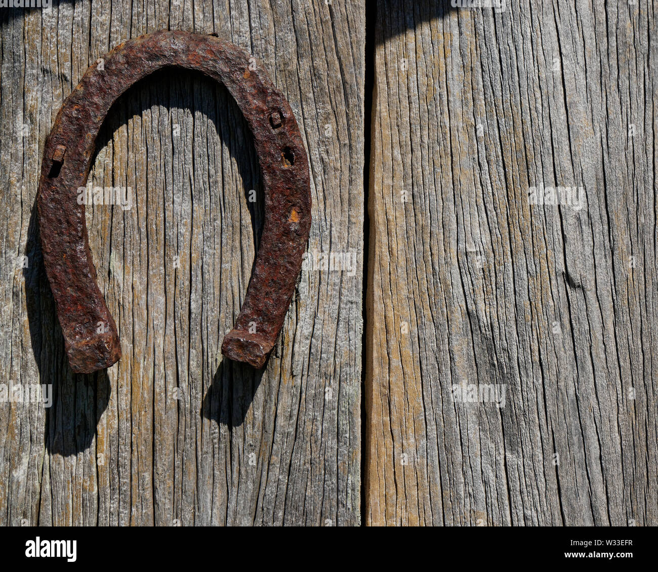 Un vecchio arrugginito ferro di cavallo appeso a testa in giù su un fienile rustico parete. Foto Stock