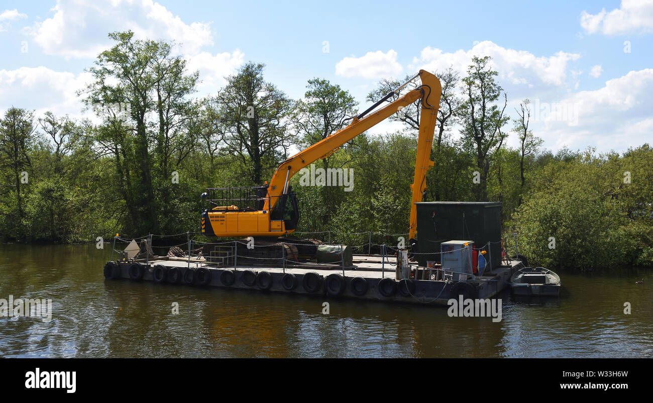 Grande escavatore meccanico sul pontone galleggiante per la manutenzione del fiume Foto Stock