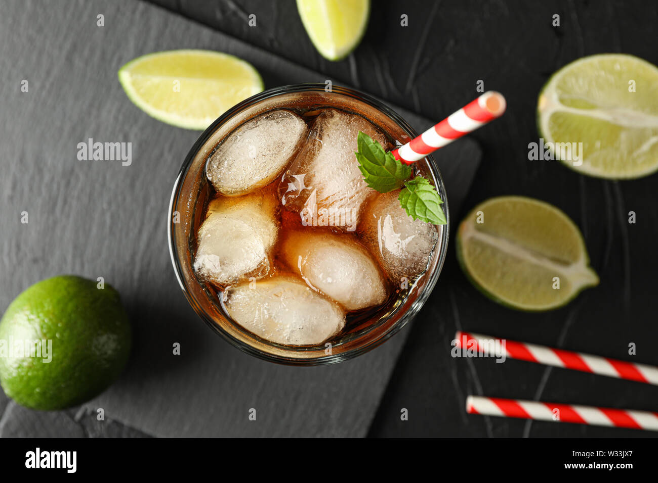 Bicchiere con ghiaccio cola di tubuli e su sfondo nero con limette Foto Stock