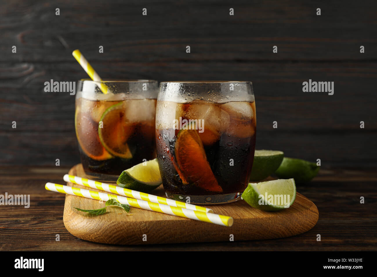 Bicchieri con ghiaccio cola, fettine di lime e di tubuli su sfondo di legno Foto Stock