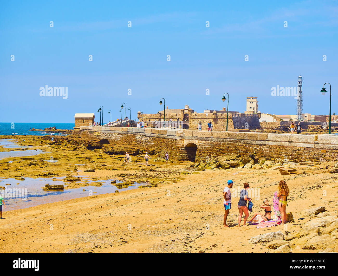 Per coloro che godono di una tintarella in La Caleta Beach con il San Sebastian Castello, una fortezza di La Caleta isola, in background. Cadice. Spagna. Foto Stock