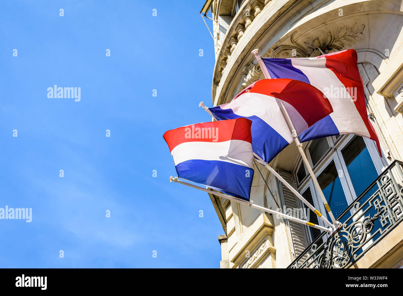 Basso angolo vista di tre francesi bandiere al vento, decking un edificio haussmanniano a Parigi, Francia, su una soleggiata giornata estiva. Foto Stock