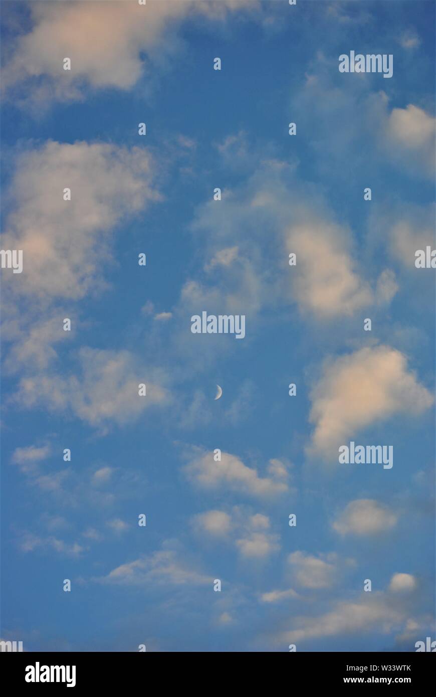 Luna crescente nelle ore diurne con nuvole bianche ed un cielo blu Foto Stock