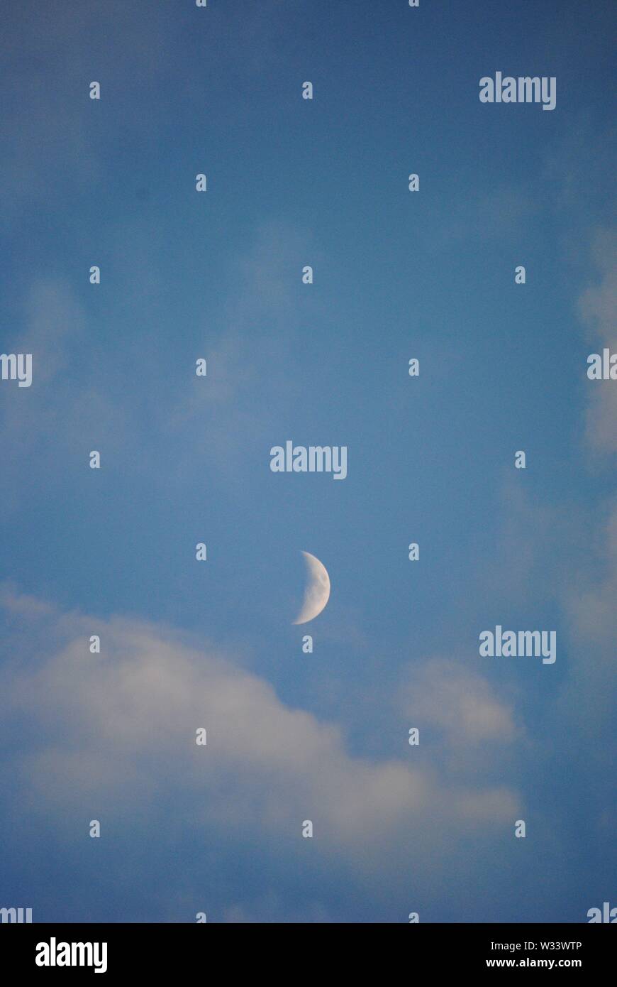 Luna crescente nelle ore diurne con nuvole bianche ed un cielo blu Foto Stock