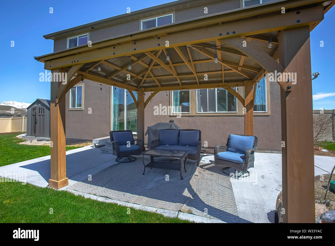 Tavolo e sedie in un patio ombreggiato da un padiglione con stringa di lampadine. Un piccolo giardino in legno passo può essere visto accanto alla casa. Foto Stock