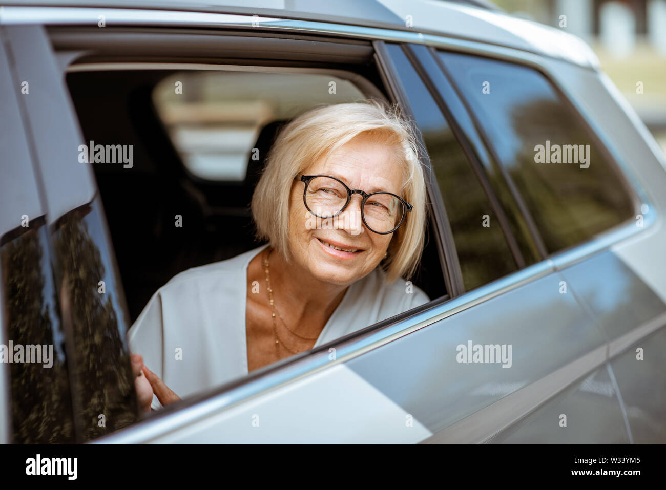 Ritratto di un felice senior business donna guardando fuori dalla finestra auto, viaggiare sul sedile posteriore di un taxi Foto Stock