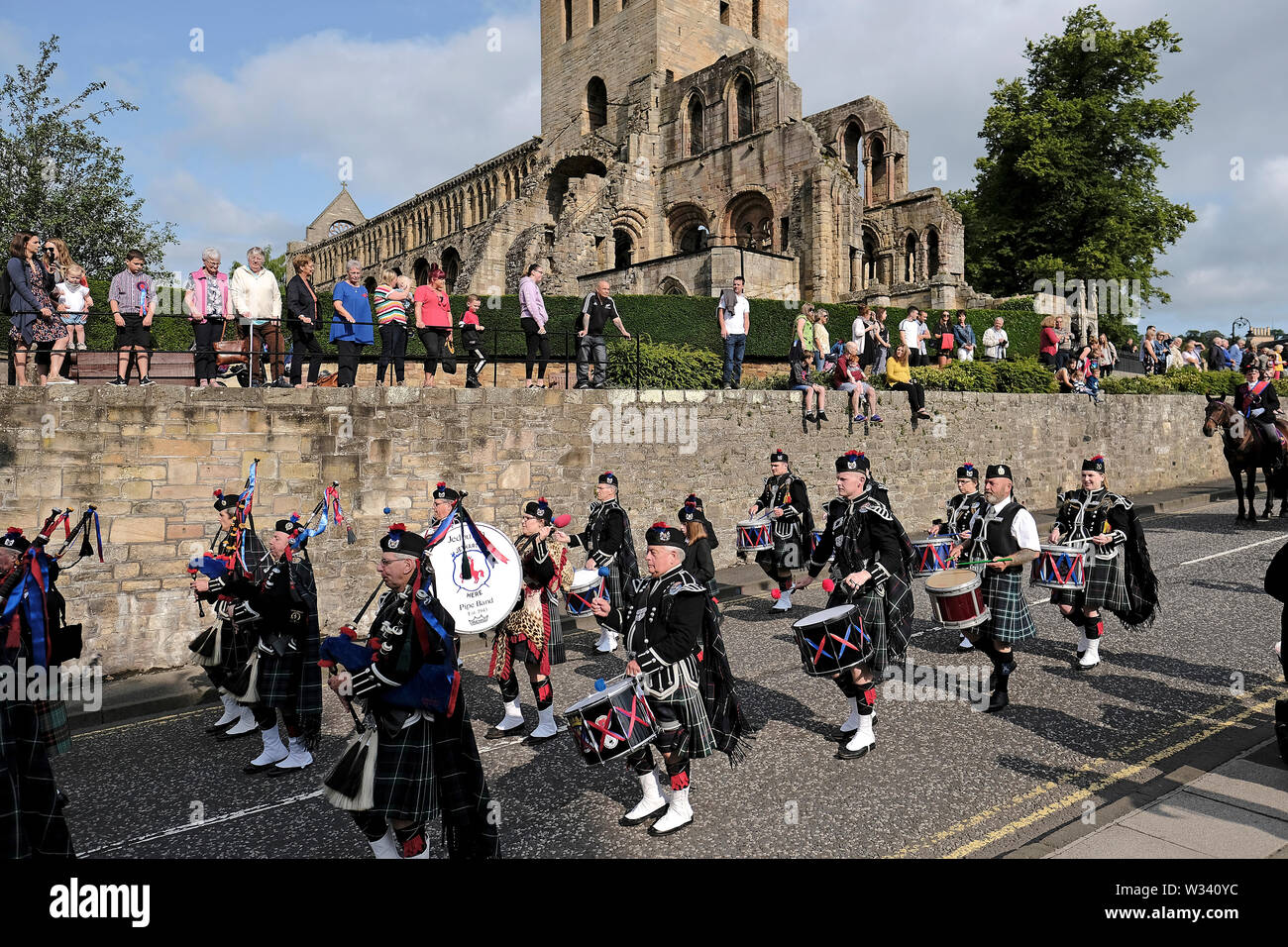 Jedburgh, Scotland, Regno Unito. 12 luglio 2019. Jethart Callant Festival del giorno Jedforest Pipe Band giocare davanti a la cavalcata, passando le rovine di Jedburgh Abbey, Jedburgh durante il Jethart Callant Festival del giorno, un festival annuale, parte della Scottish comune stagione di equitazione, venerdì 12 luglio 2019, Jedburgh Scottish Borders, Scotland, Regno Unito. Credito di sfiato: Rob grigio/Alamy Live News Foto Stock