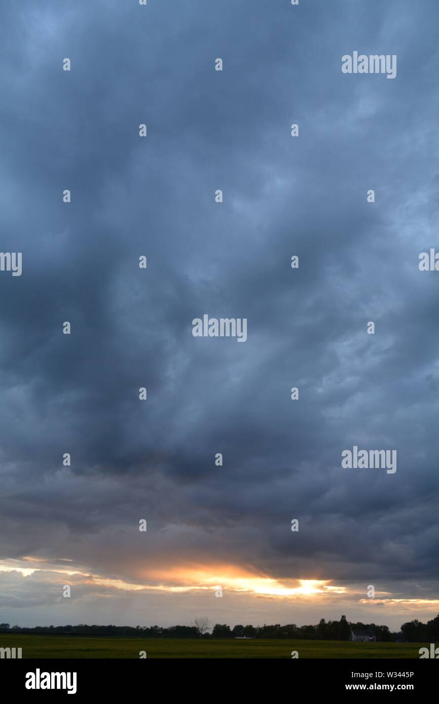 Paesaggio di swirly scure nuvole al tramonto con un bagliore dorato all'orizzonte dal sole al tramonto. Foto Stock