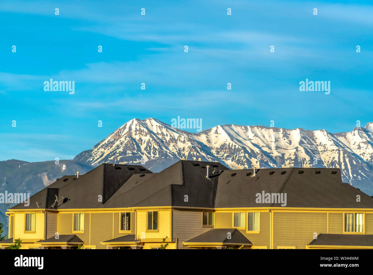 Case con la parete orizzontale didings contro la neve ha raggiunto un picco di montagna e cielo blu. Tubi di camino può essere visto o il buio i tetti delle case. Foto Stock