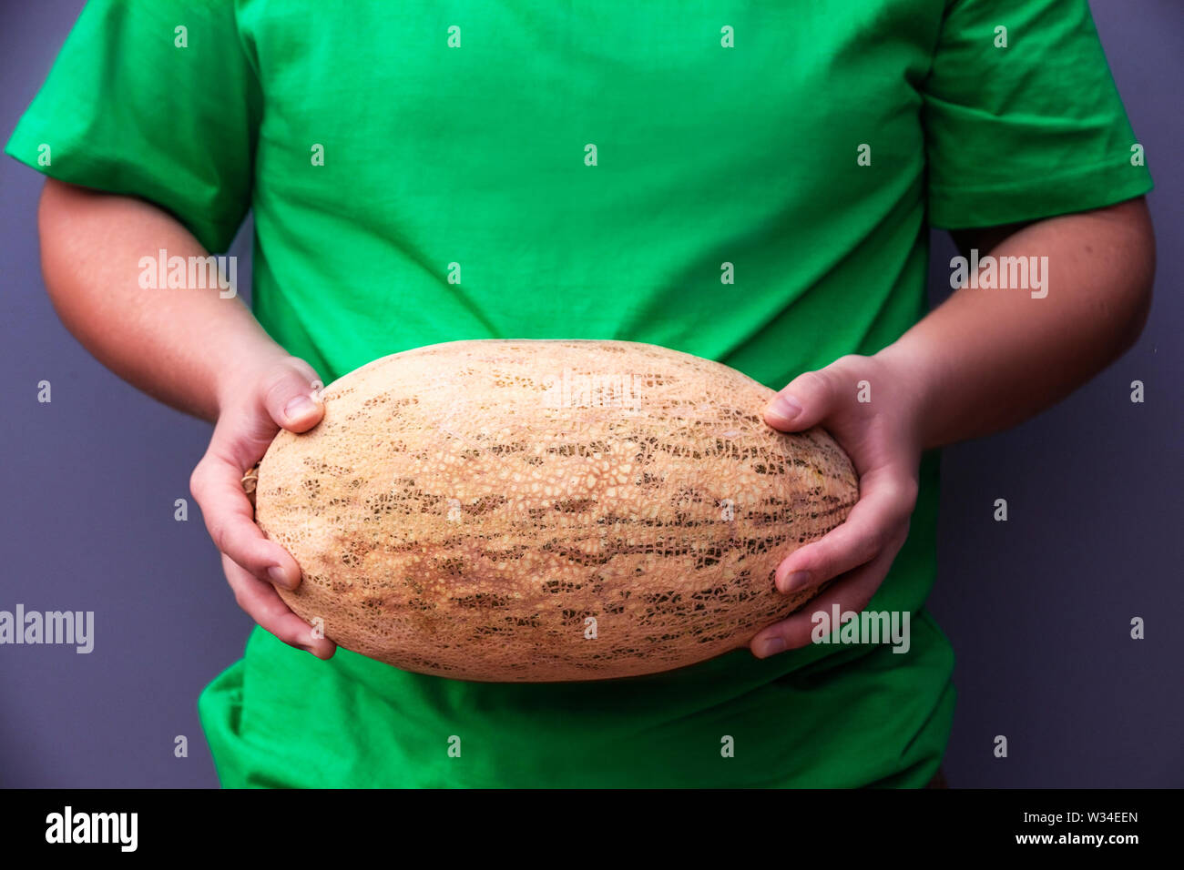Il giovane uomo è in possesso di un grande ovale arancione melone maturo. Utili prodotti agricoli. Il raccolto dal campo Foto Stock