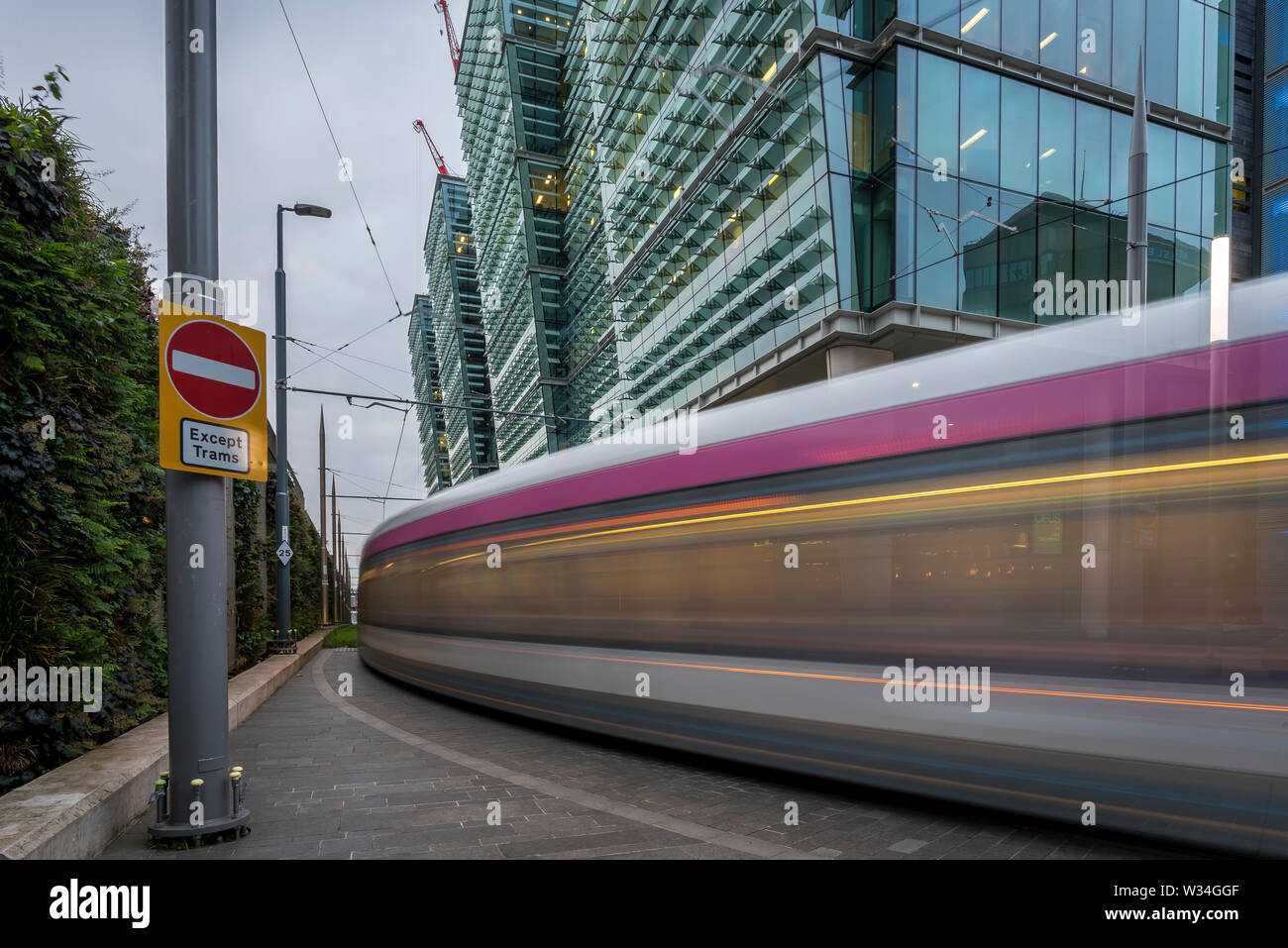 Una fermata del tram a Birmingham, Inghilterra. La fermata del tram è passato in movimento moderno, vetro frontale in edifici per uffici Foto Stock