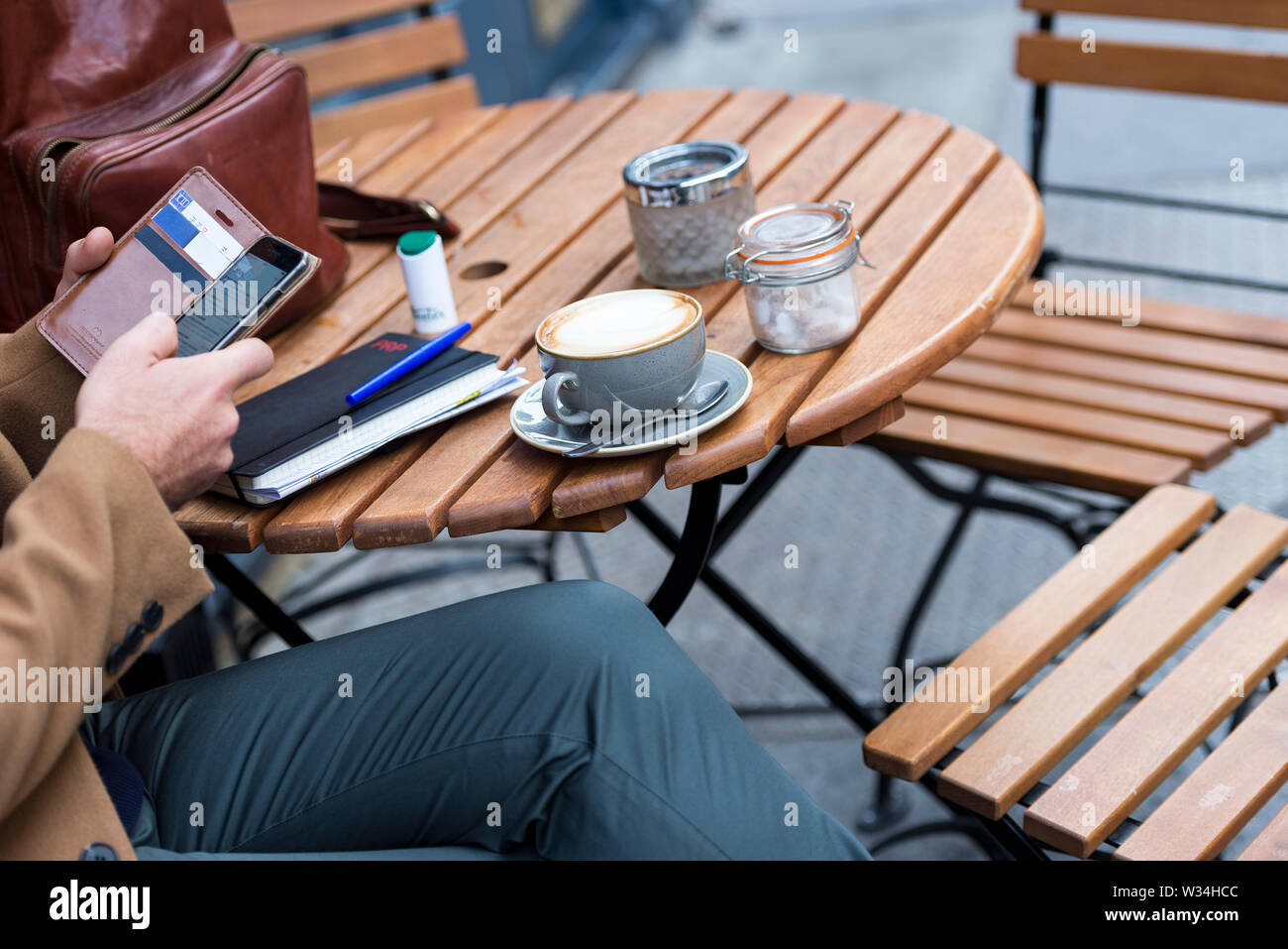 Un momento sincero di un uomo che lavora in remoto in un bar di Londra con cappuccino, smartphone e notebook su un tavolo di legno, un concetto di stile di vita urbano. Foto Stock