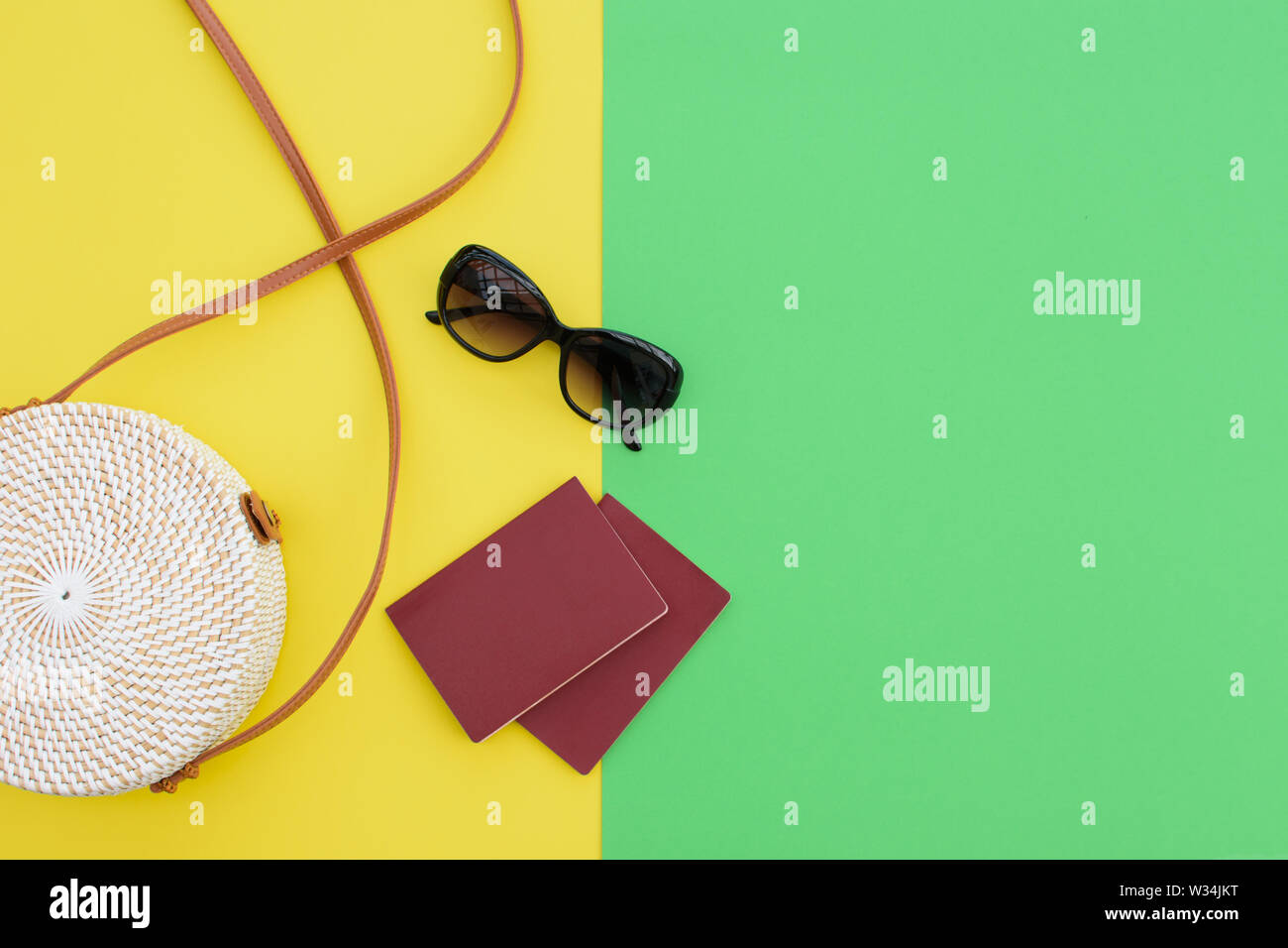 Bellissimo tondo paglia borsetta e occhiali da sole con i passaporti in giallo-verde dello sfondo. Borsa alla moda. Foto Stock