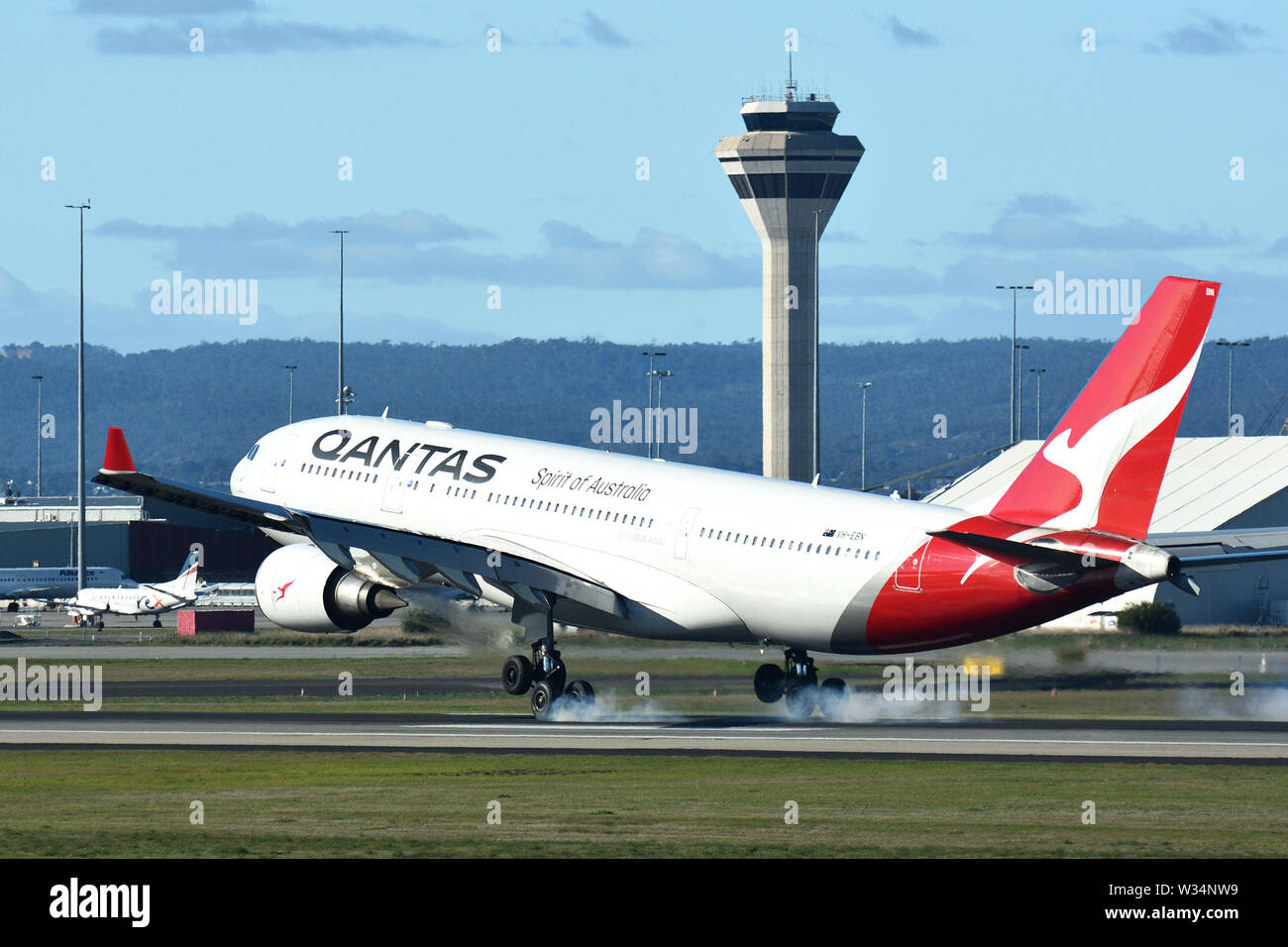 Airbus A330-200 VH-EBN della Qantas Airways atterra all'Aeroporto di Perth con fumo visibile dal carrello di atterraggio. La torre di controllo in background. Foto Stock