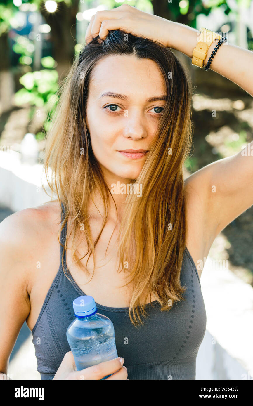 Giovane donna europea con una bottiglia di acqua dopo il jogging all'aperto in Lisabone. Indossa un coperchio grigio e una luce gambali dello sport Foto Stock