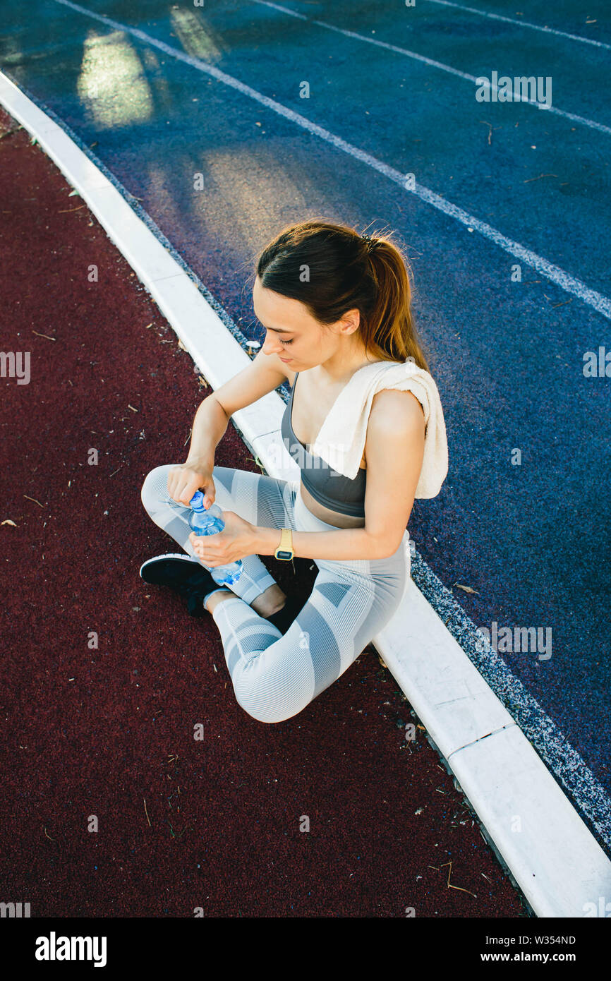 Giovane donna con una bottiglia di acqua dopo il jogging all'aperto in Lisabone. Indossa un coperchio grigio e una luce gambali dello sport Foto Stock