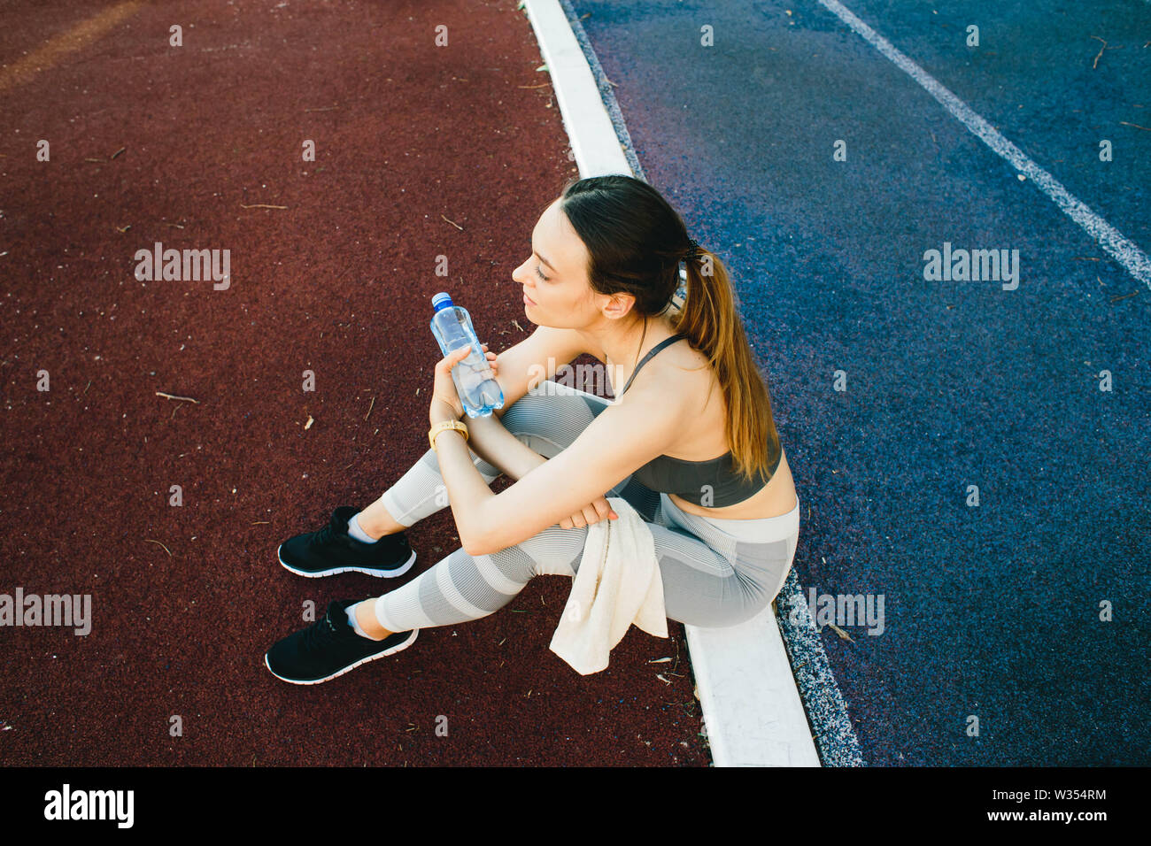 Giovane donna con una bottiglia di acqua dopo il jogging all'aperto in Lisabone. Indossa un coperchio grigio e una luce gambali dello sport Foto Stock
