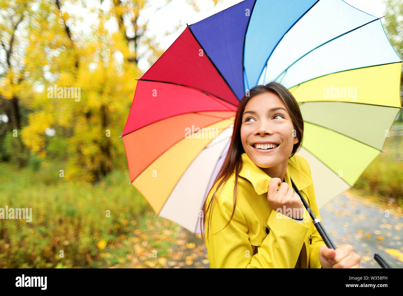 Autunno / autunno - donna felice con ombrello in caso di pioggia a piedi nella foresta. Ragazza godendo di caduta di pioggia giorno guardando lontano sorridente. Razza mista Caucasian / asiatica ragazza cinese. Foto Stock