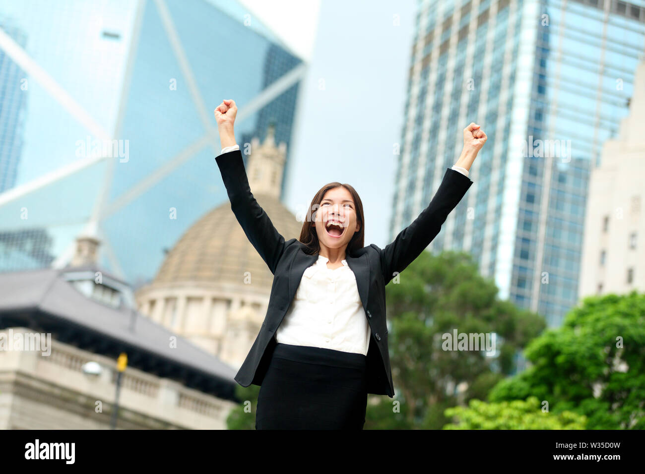 Il successo del business - celebrando imprenditrice a Hong Kong il tifo gli obiettivi aziendali con le braccia sollevate fino come vincitore. Giovani razza mista cinese / asiatici caucasica professionale femminile in Hong Kong Central. Foto Stock