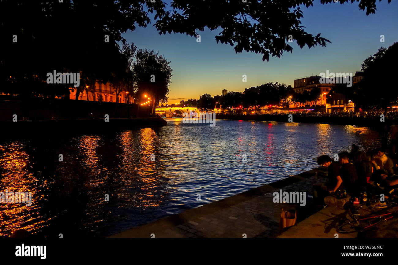 La gente celebra vicino al Pont Marie ponte illuminato di notte Ile Saint Louis, presso il fiume Senna, Parigi, Francia. Foto Stock