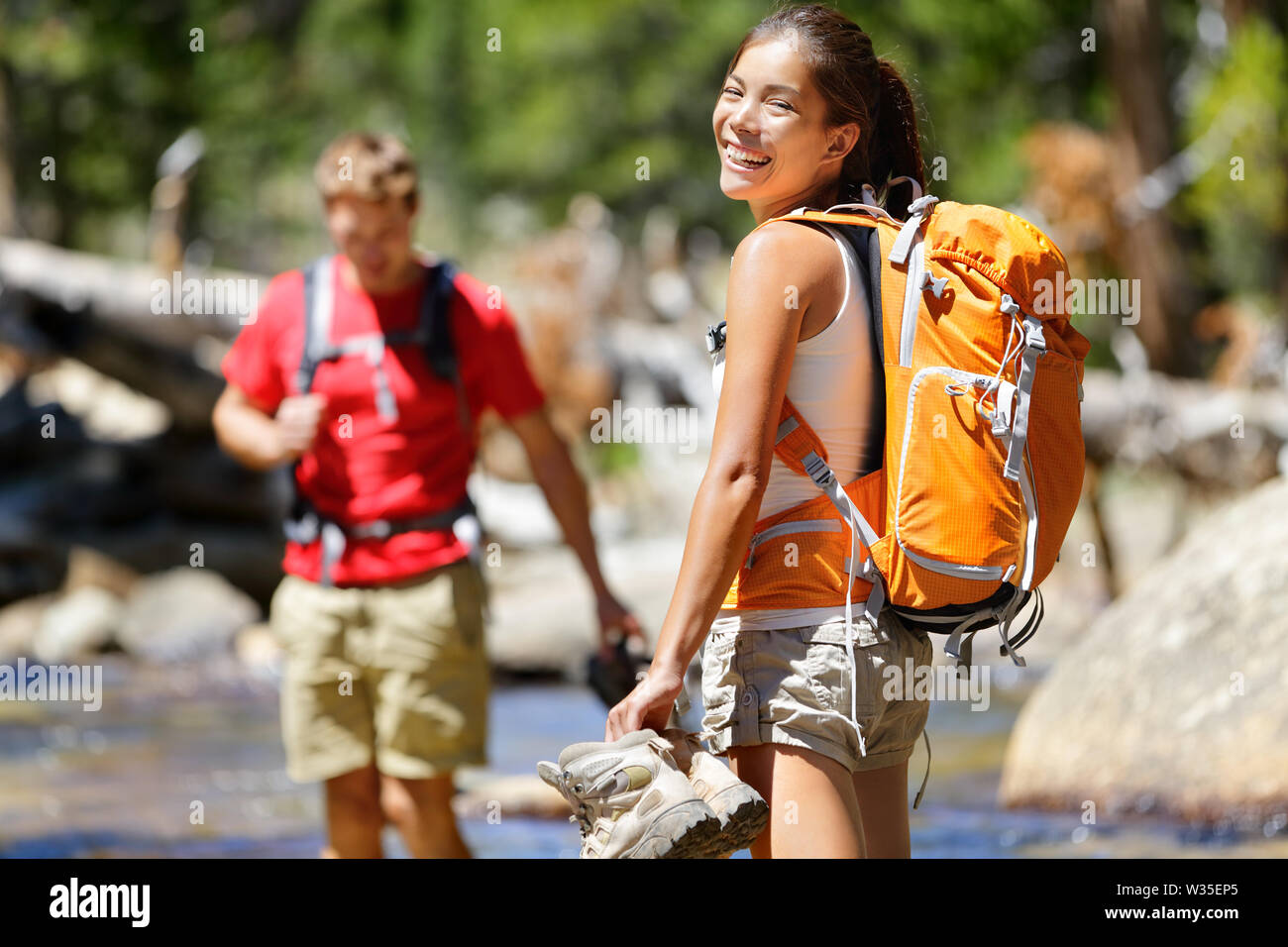 Escursionismo amici divertendosi Varcando il fiume nella foresta. Giovani adulti felice camminare a piedi nudi in acqua con i piedi bagnati su un viaggio avventura escursione in natura. Foto Stock