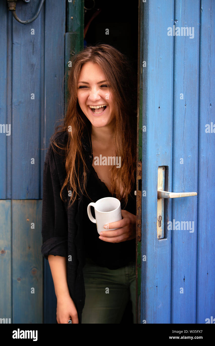 Ritratto di giovane donna bruna coppa di ritegno e di stare alla porta blu Foto Stock