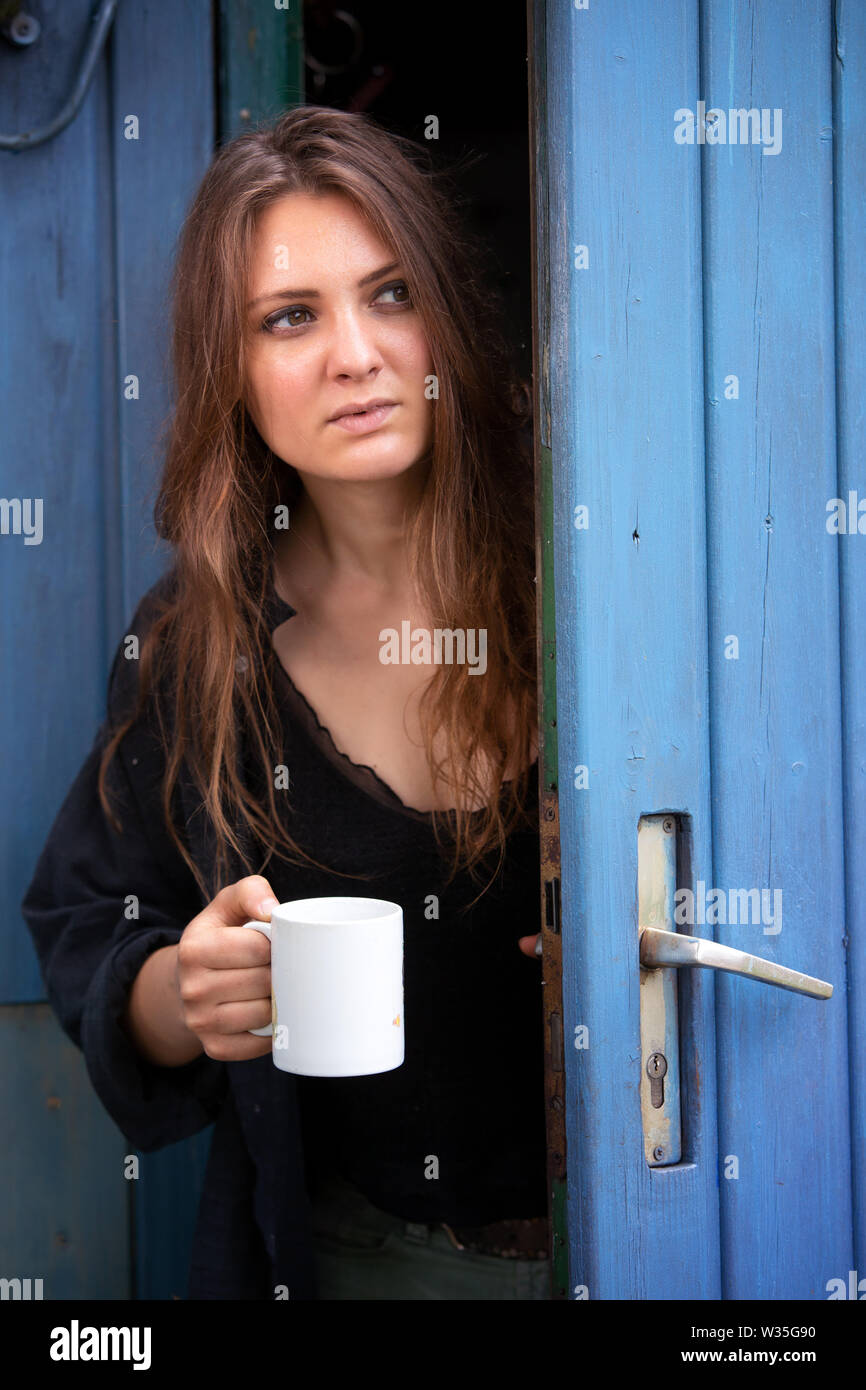 Ritratto di giovane donna bruna coppa di ritegno e di stare alla porta blu Foto Stock