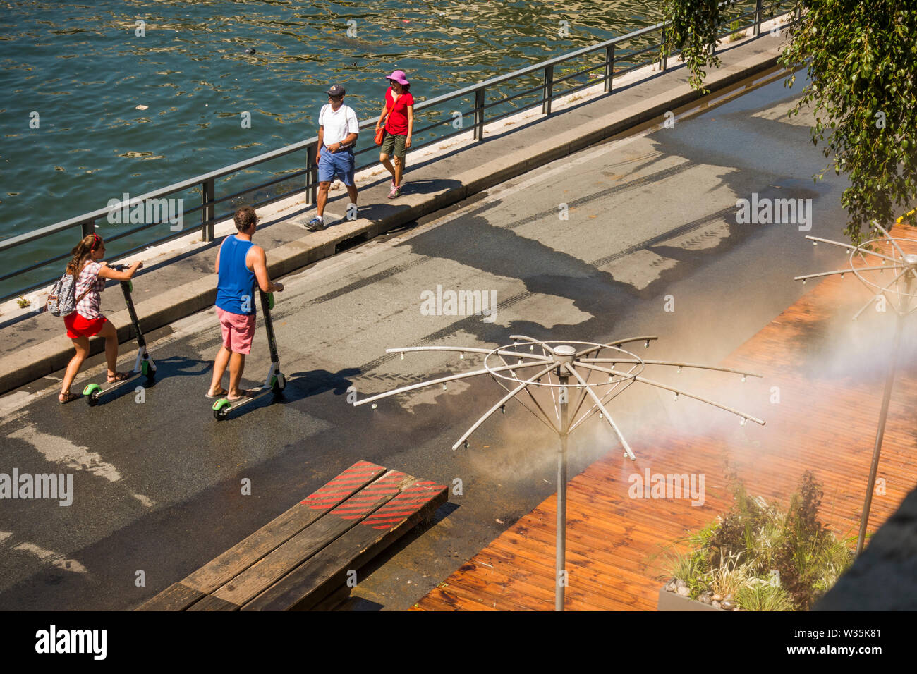 I pedoni a camminare lungo il fiume Senna ottenere sollievo da sprinkler acqua, durante l'ondata di caldo. Parigi, Francia. Foto Stock