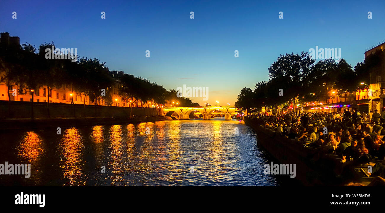 La gente celebra vicino al Pont Marie ponte illuminato di notte Ile Saint Louis, presso il fiume Senna, Parigi, Francia. Foto Stock