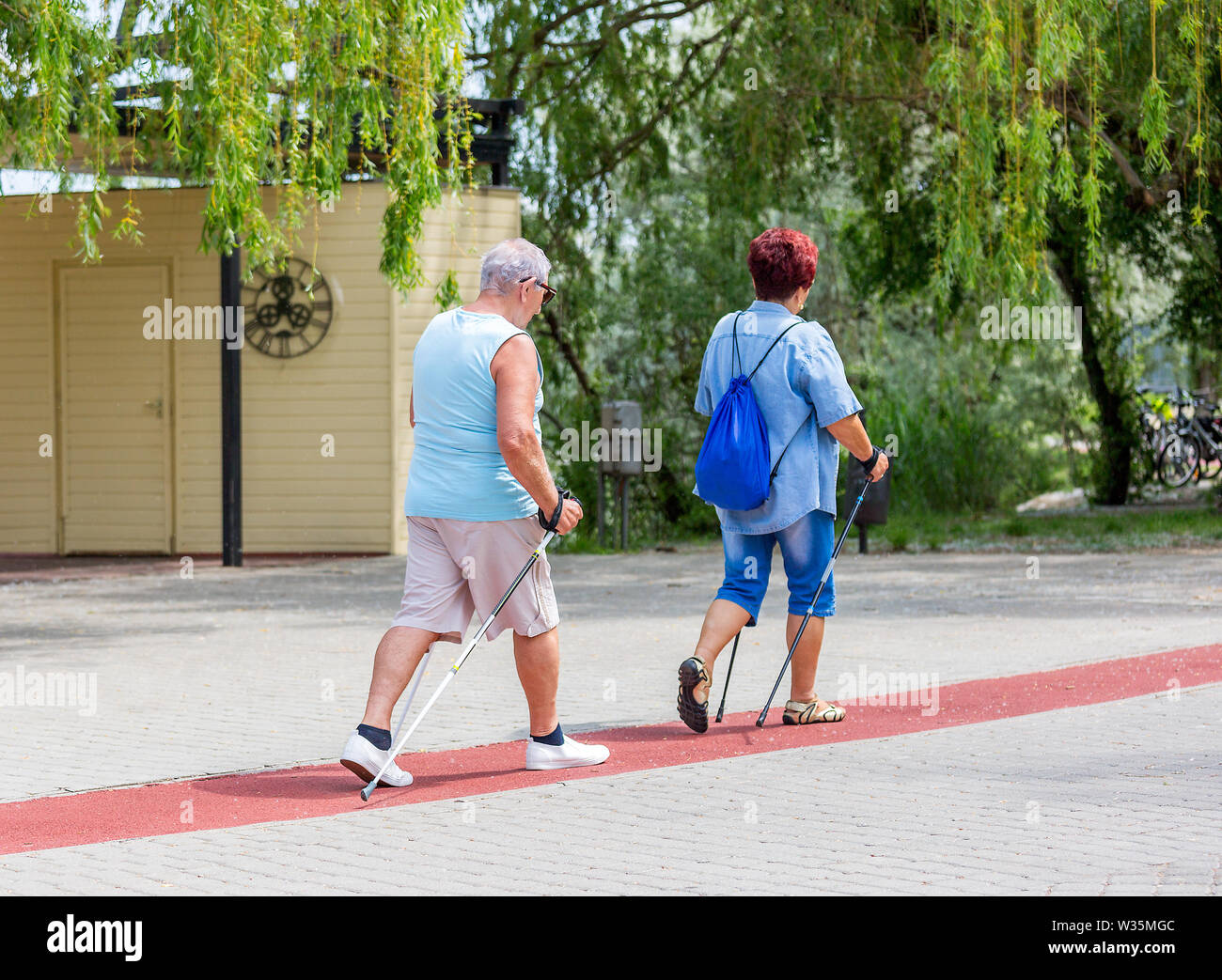 Coppia senior a piedi con i bastoni per escursioni sul tapis roulant lungo un lago nel parco della città Foto Stock