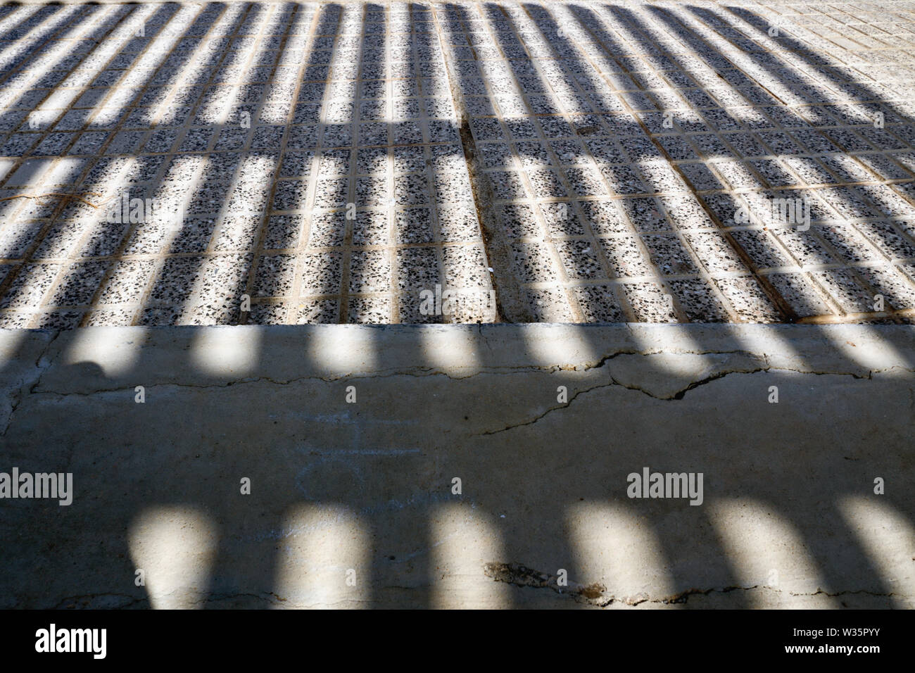 Extreme shadowing in forma di formazione del reticolo su una strada e un pezzo di marciapiede, in presenza di intensa luce solare. Close-up in diverse tonalità di grigio. Foto Stock