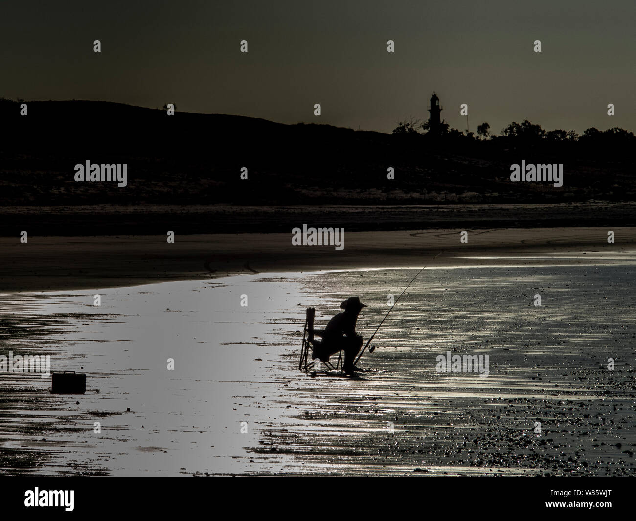 Silhouette di un uomo seduto in una sedia da campeggio e la pesca in un drammatico retroilluminazione Foto Stock