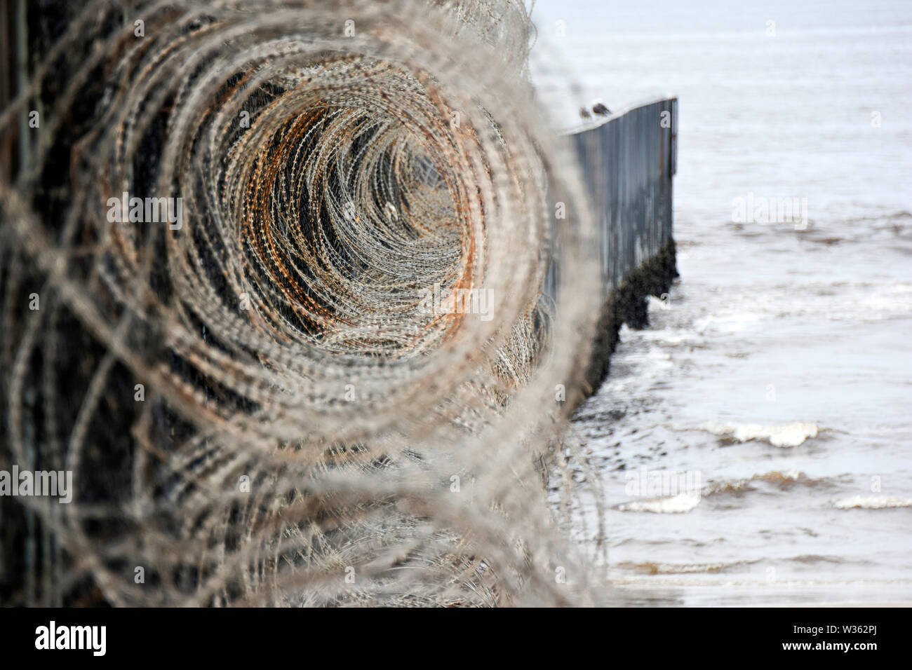 Filo di concertina lungo il lato degli Stati Uniti di primaria barriera di frontiera a San Diego, California, dove si corre nell'Oceano Pacifico. Foto Stock