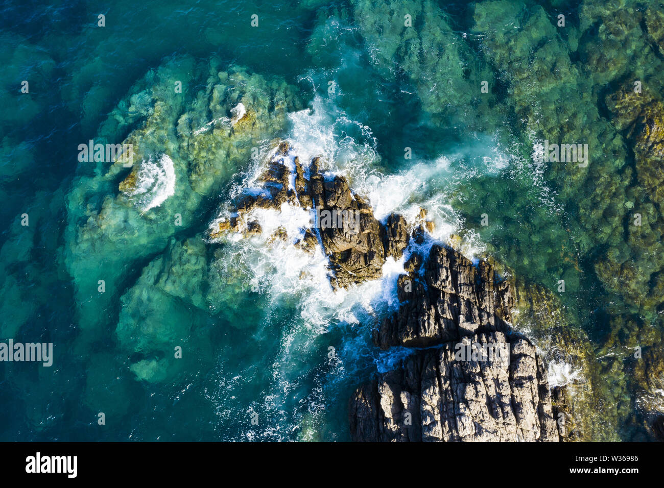 Vista da sopra, splendida vista aerea di alcune onde che si infrangono su una costa rocciosa durante una giornata di vento in Sardegna, Italia. Foto Stock
