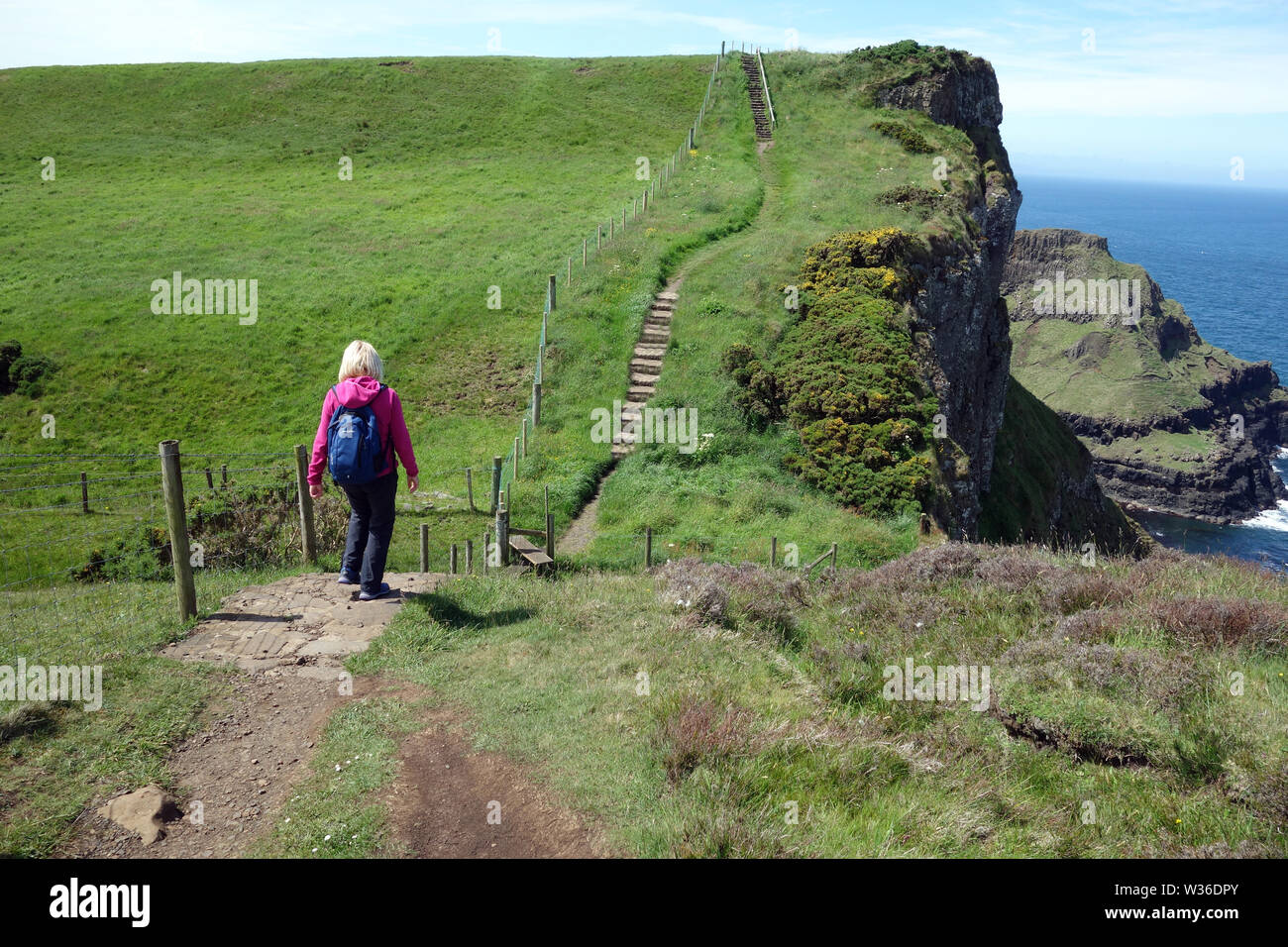 Donna che cammina verso passaggi sulla Giant's Causeway sentiero costiero, County Antrim, Irlanda del Nord, Regno Unito Foto Stock