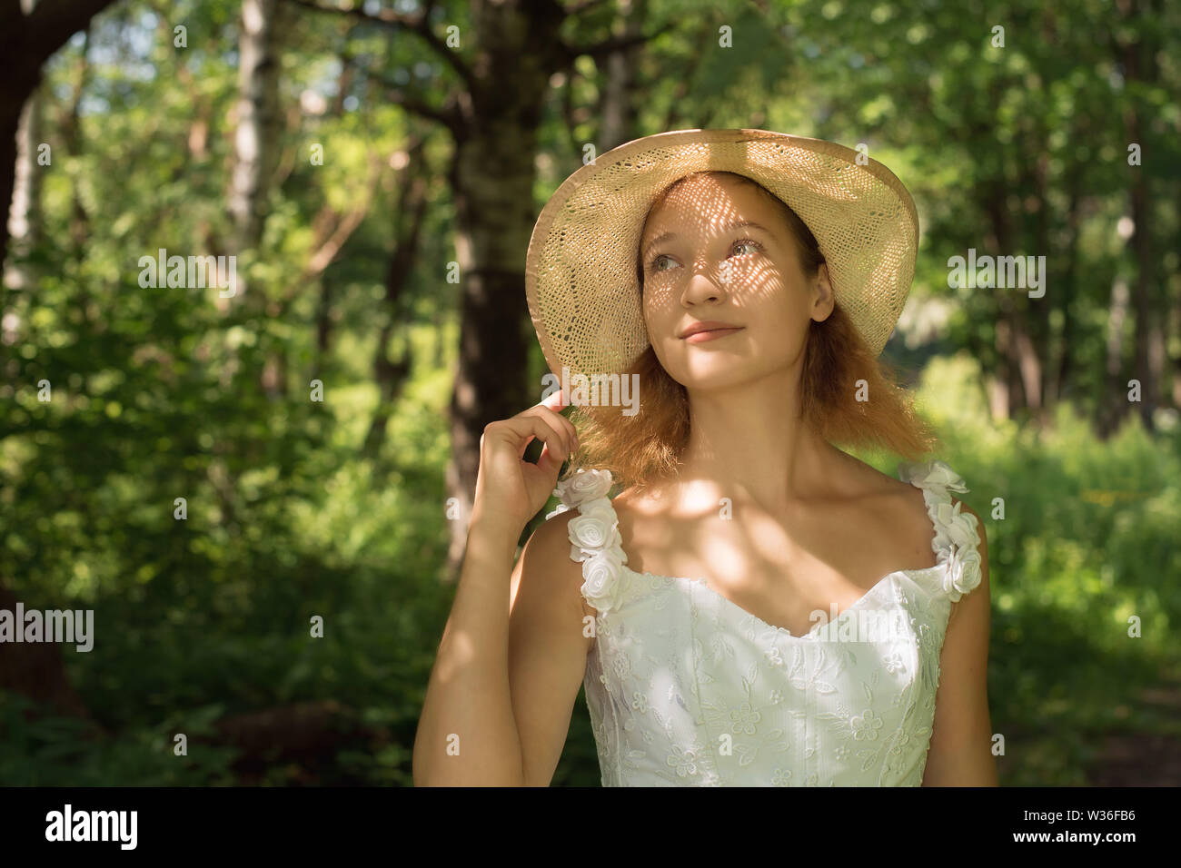 Ragazza in un cappello di paglia nella foresta in una giornata di sole con un cesto di frutta Foto Stock