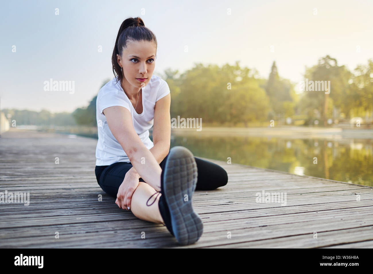 Ritratto di giovane donna stretching vicino al lago prima di fare jogging al mattino Foto Stock