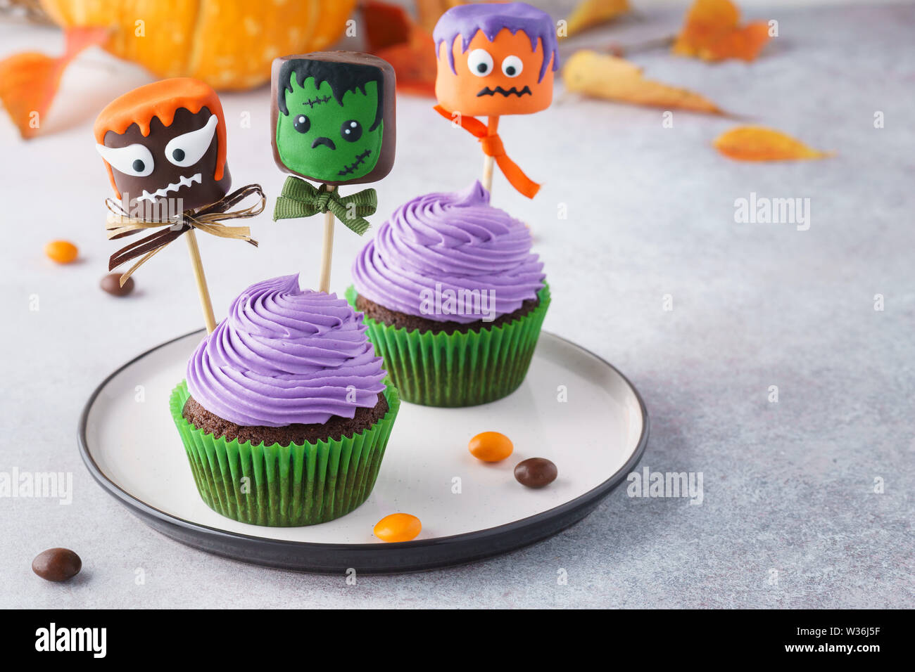 Tortini di Halloween e pop di torta al cioccolato o marshmallow anabbaglianti con divertenti monster facce. Messa a fuoco selettiva, copia dello spazio. Foto Stock