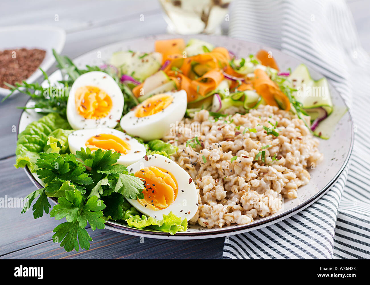 La colazione ciotola con i fiocchi d'avena, zucchine, lattuga, carota e uova sode. Insalata fresca. Cibo sano. Vegetariano ciotola di buddha. Foto Stock