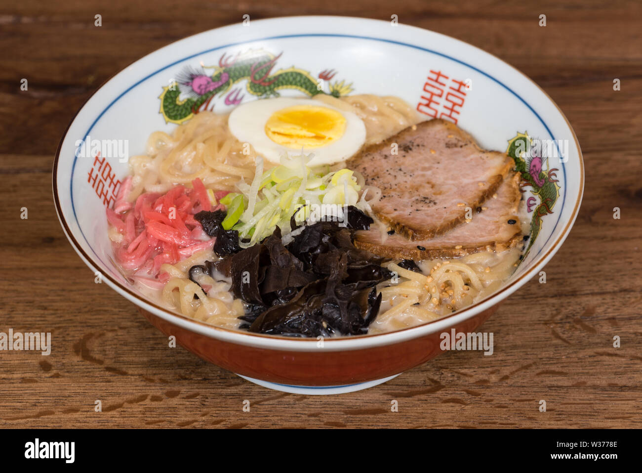 Ramen tonkotsu con carne di maiale, latte di soia, brodo di carne di maiale, funghi neri, uova, cipolle, servita in una ciotola di legno scuro dello sfondo della tabella Foto Stock