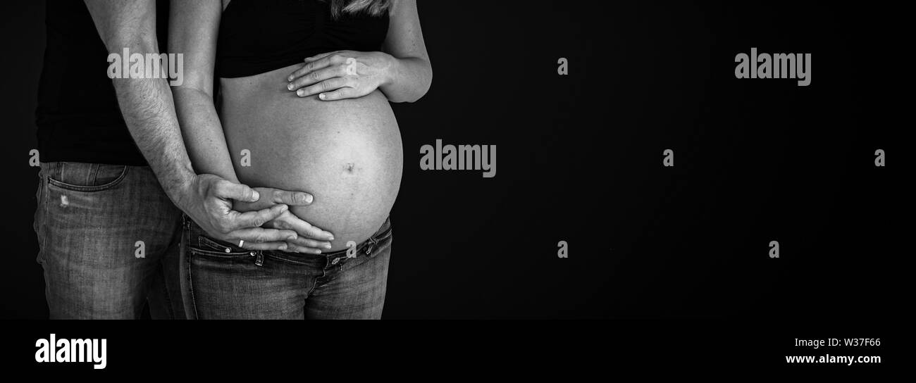 Pancia in gravidanza giovane tenendo le mani attorno a baby bump sfondo nero Foto Stock