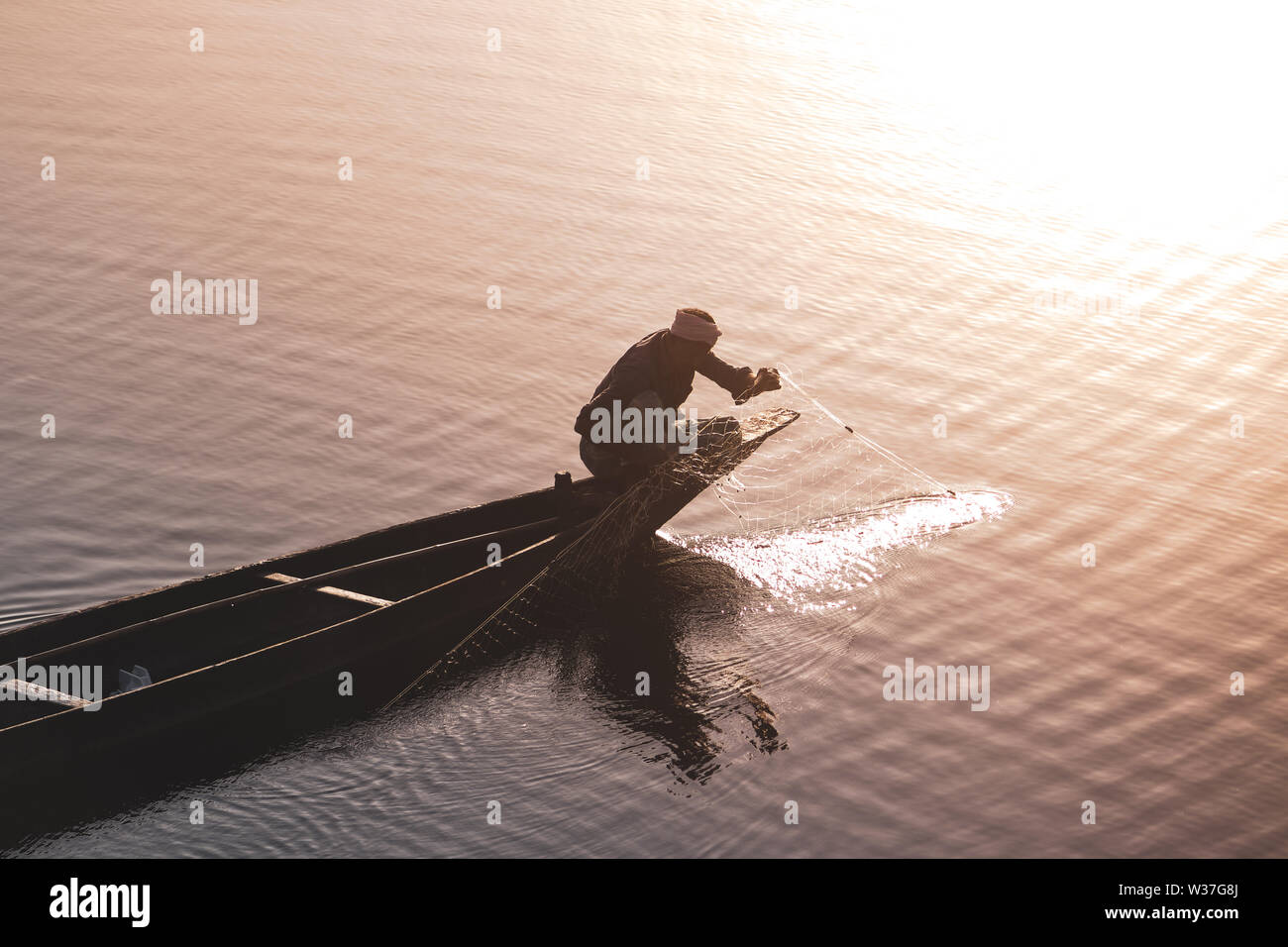 Uomo di pesca sul lago da una barca durante il tramonto Foto Stock