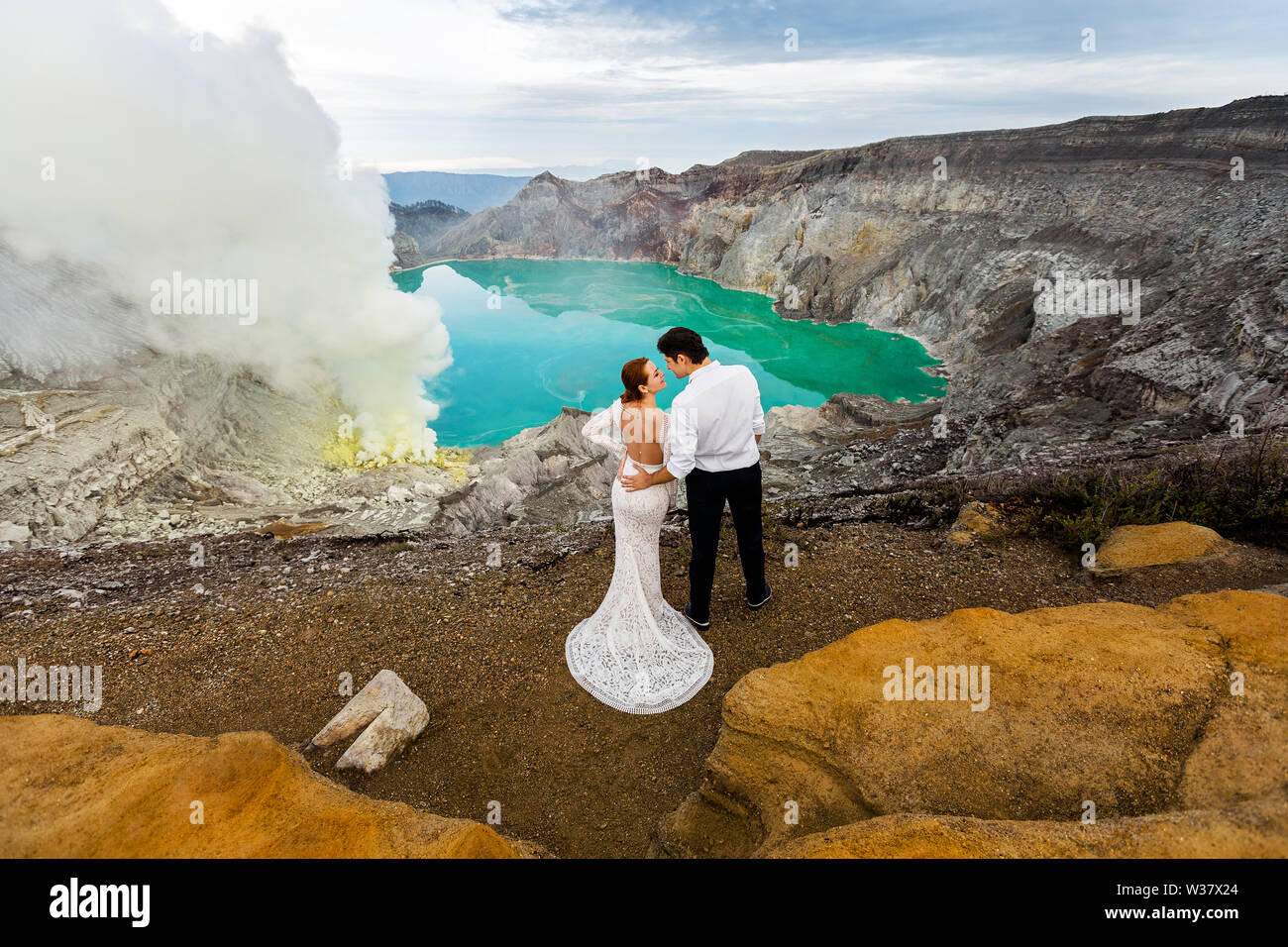 Sposa e lo sposo abbraccio in piedi nel cratere di un vulcano su uno sfondo di colore verde e il lago vulcanico solforico fumo Foto Stock