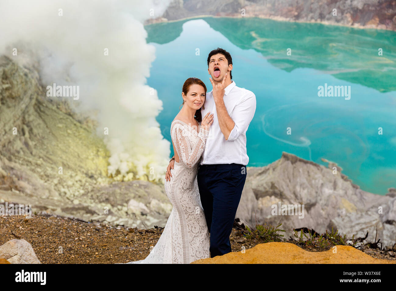 La sposa e lo sposo si divertono nel cratere del vulcano sullo sfondo di verde acido solforico lago vulcanico e fumo. Foto Stock