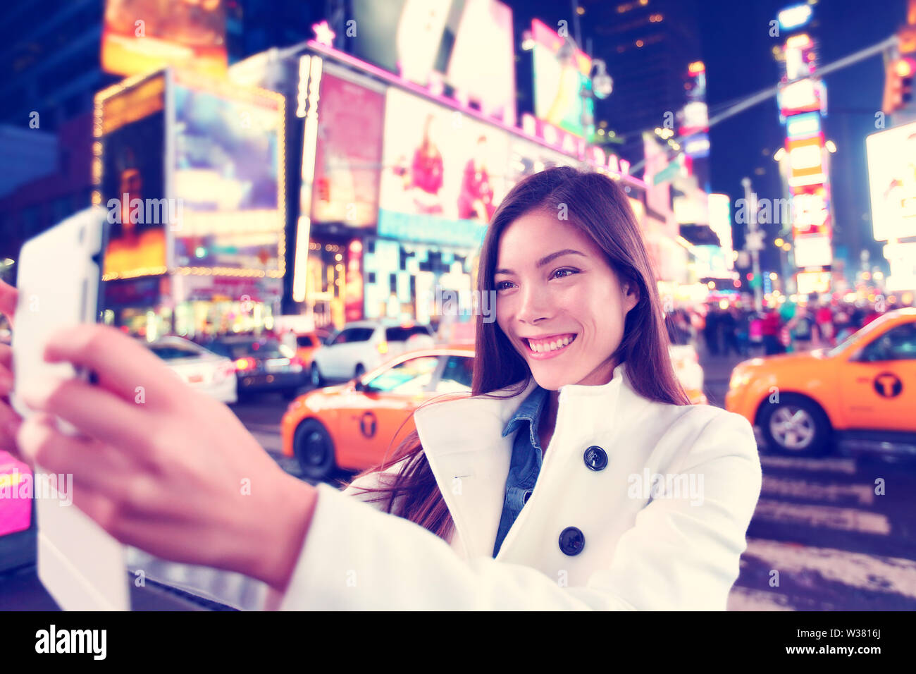 Donna felice turistica prendendo foto selfie con la compressa nella città di New York Manhattan, Times Square. Multietnica caucasico asiatica donna nella sua 20s gioiosi e sorridenti indossando la molla pea coat. Foto Stock