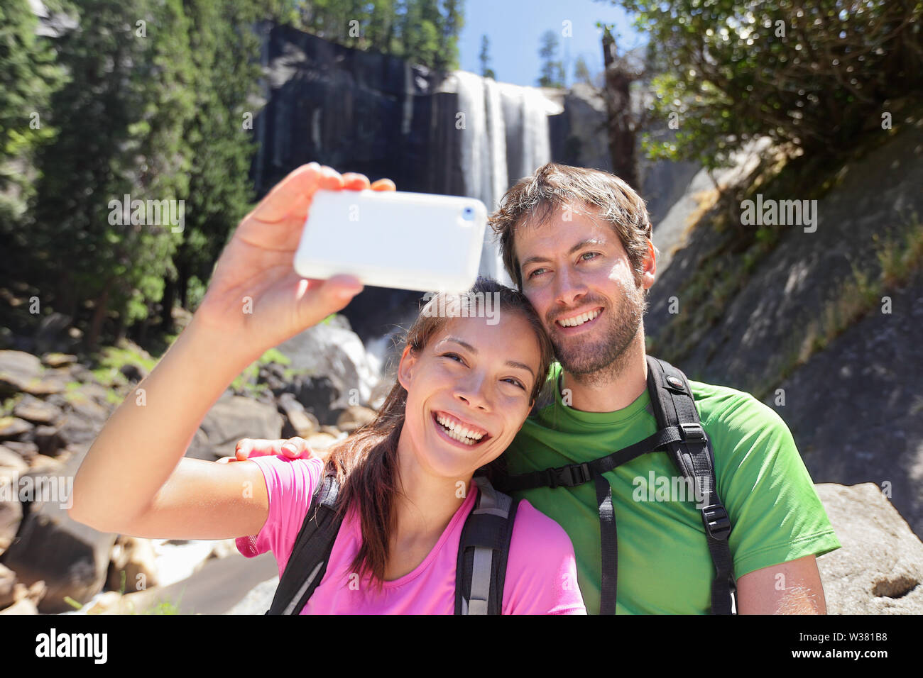 Uno stile di vita attivo coppia di escursionisti escursioni al Parco Nazionale di Yosemite prendendo un autoritratto foto con smartphone di cascata, caduta primaverile. Giovani escursionismo giovane rilassarsi in estate natura paesaggio. Foto Stock